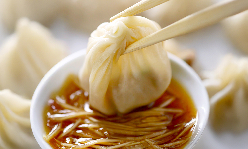 Xiao long bao dipped into vinegar and ginger slices